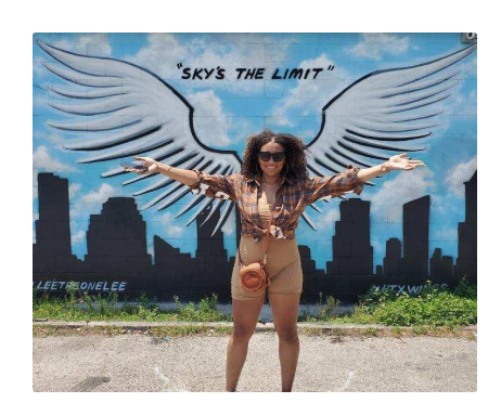 Woman smiling in front of "Sky's The Limit" mural